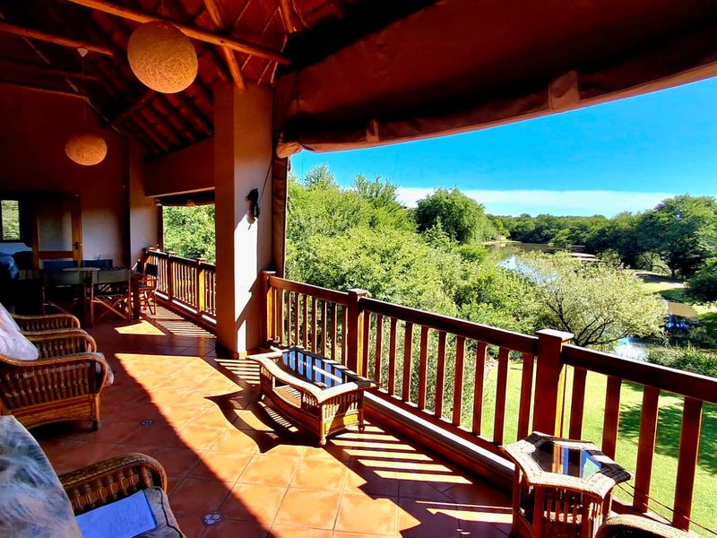 Spacious covered patio featuring tiled flooring, a wooden balustrade, and exposed timber rafters, offering scenic views of the surrounding garden and river.