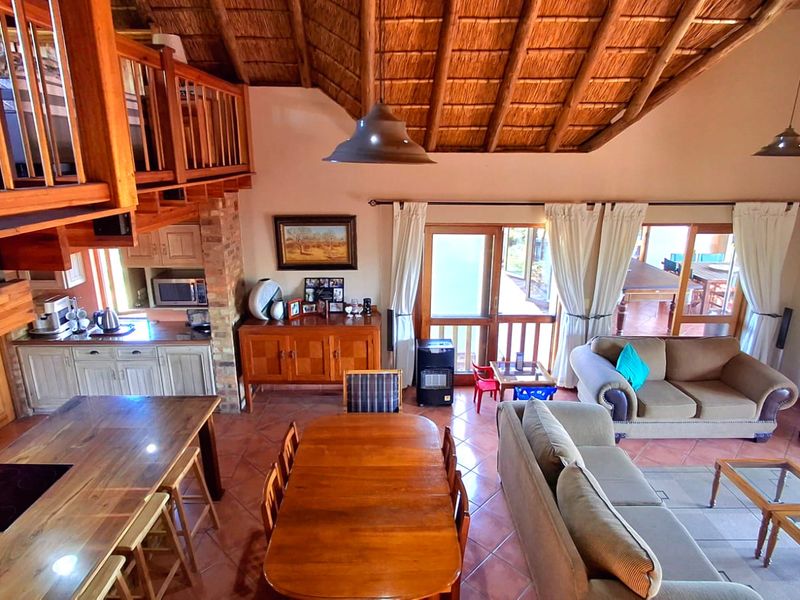 Spacious open-plan living area featuring a high vaulted thatch ceiling, exposed timber beams, a mezzanine level, and direct access to the outdoor patio.