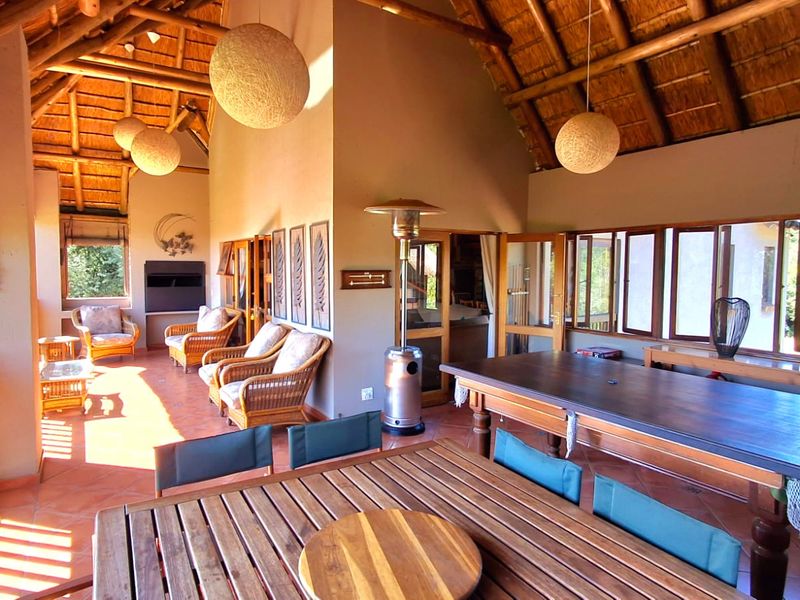 Spacious covered patio featuring a high thatched roof with exposed timber rafters, terracotta flooring, and a built-in fireplace, offering an ideal outdoor entertainment area.