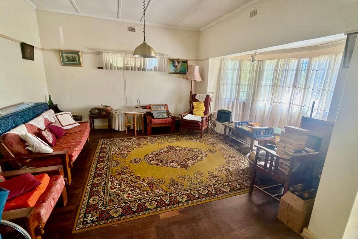A spacious living room featuring a large bay window, original picture rails, and hardwood flooring, offering a classic foundation for renovation.
