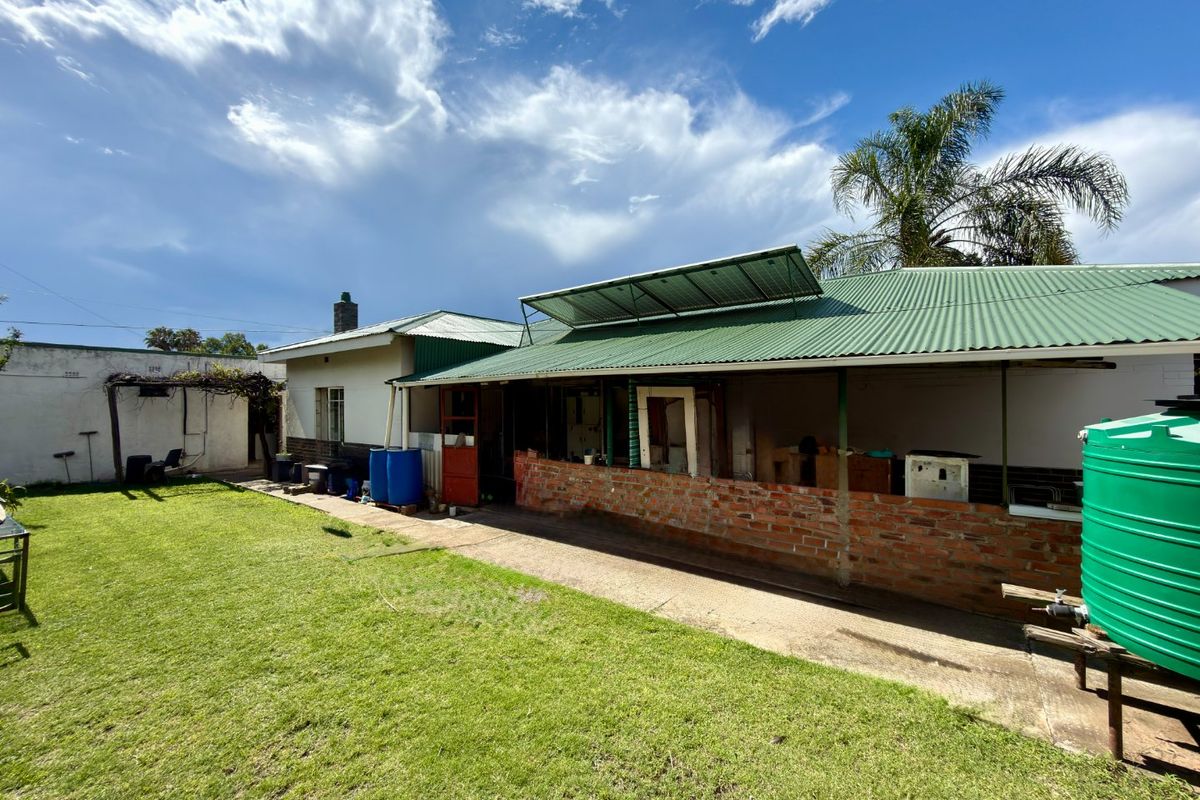 Rear view of the property featuring a corrugated metal roof with solar panels, a brick-walled patio area, and a spacious garden with a water tank.