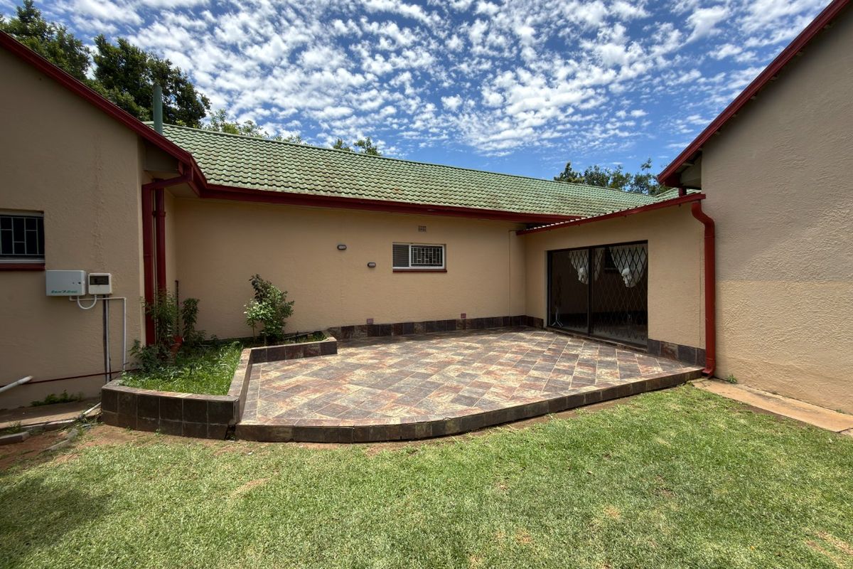 Rear exterior view featuring a paved patio area, raised garden bed, and access to the home via a sliding door with security gate.
