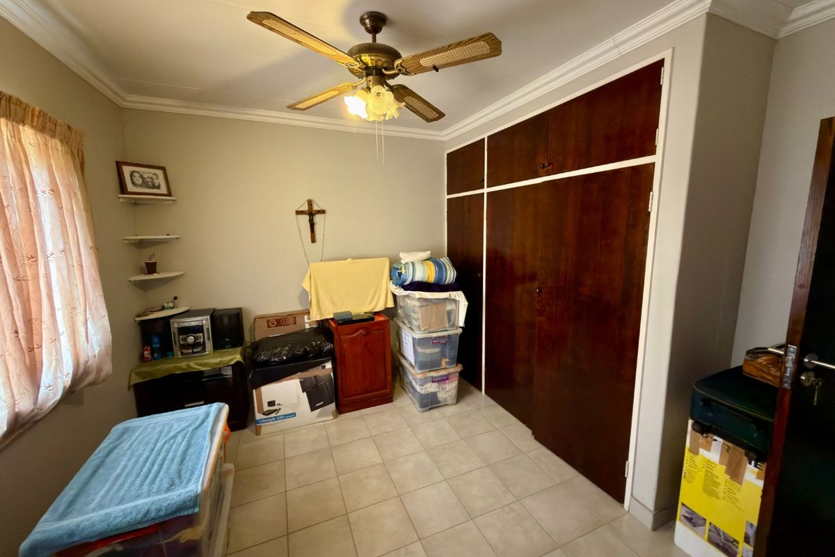 A bedroom featuring tiled flooring, a ceiling fan, and built-in wooden cupboards, offering a functional space with potential for modernization.