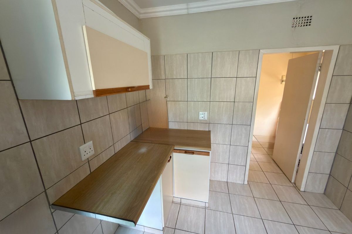 A compact, empty kitchen featuring tiled walls and floors, laminate countertops, and built-in cabinetry, offering a functional space ready for modernization.