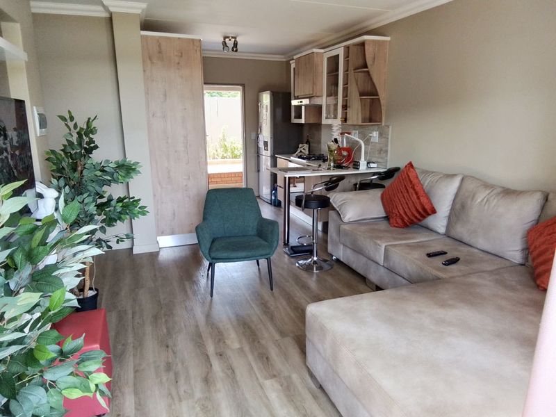 Open-plan living area featuring modern laminate flooring, a compact kitchen with breakfast bar, and direct access to an outdoor space.