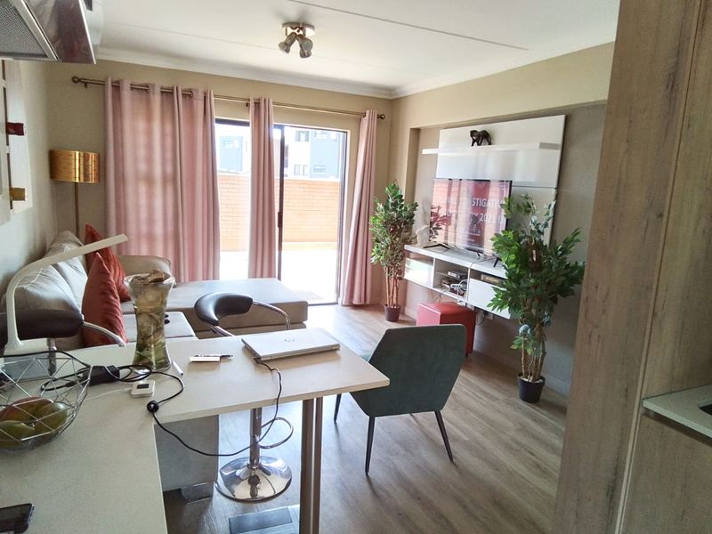 Open plan living area featuring laminate flooring, a built-in media unit, and a sliding glass door providing access to the outdoor patio.