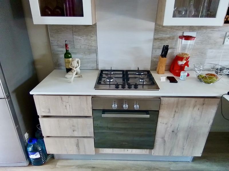 A compact kitchen area featuring a built-in gas hob, oven, light wood-finish cabinetry, and a modern tiled backsplash.