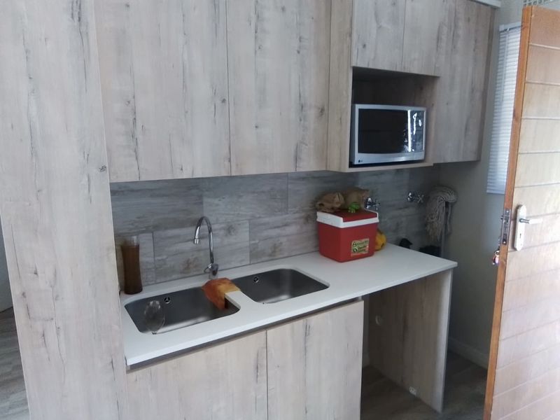 A functional scullery area featuring modern wood-look cabinetry, a double stainless steel sink, tiled backsplash, and a built-in microwave space.