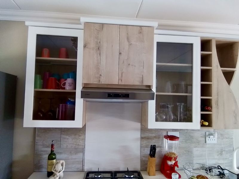 Modern kitchen featuring light wood and white cabinetry, glass-fronted display cupboards, a built-in extractor fan, and a tiled splashback above the gas hob.