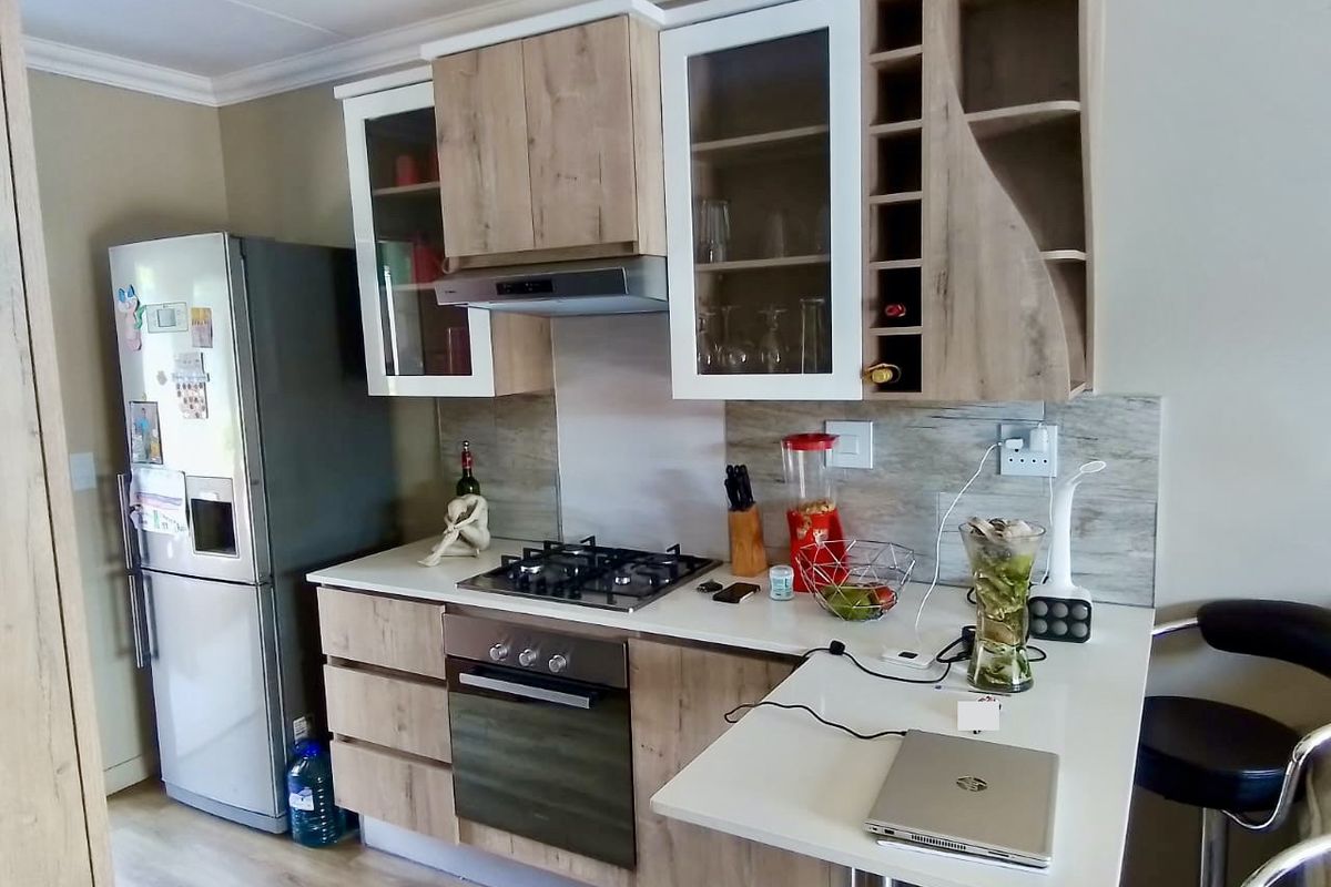 Modern kitchen featuring light wood-tone cabinetry, integrated gas hob, built-in oven, extractor fan, and a breakfast bar extension with laminate countertops.