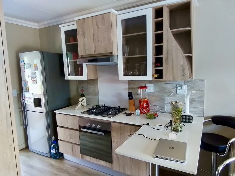 Modern kitchen featuring light wood-tone cabinetry, integrated gas hob, built-in oven, extractor fan, and a breakfast bar extension with laminate countertops.