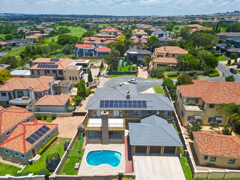 Aerial view of a residential property featuring a tiled roof with solar panels, a swimming pool, and a paved driveway in a suburban estate.