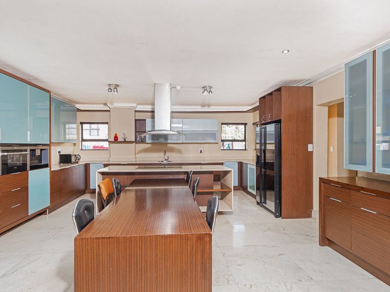 Spacious modern kitchen featuring extensive built-in cabinetry, a large central island, stone countertops, and integrated appliances with tiled flooring throughout.