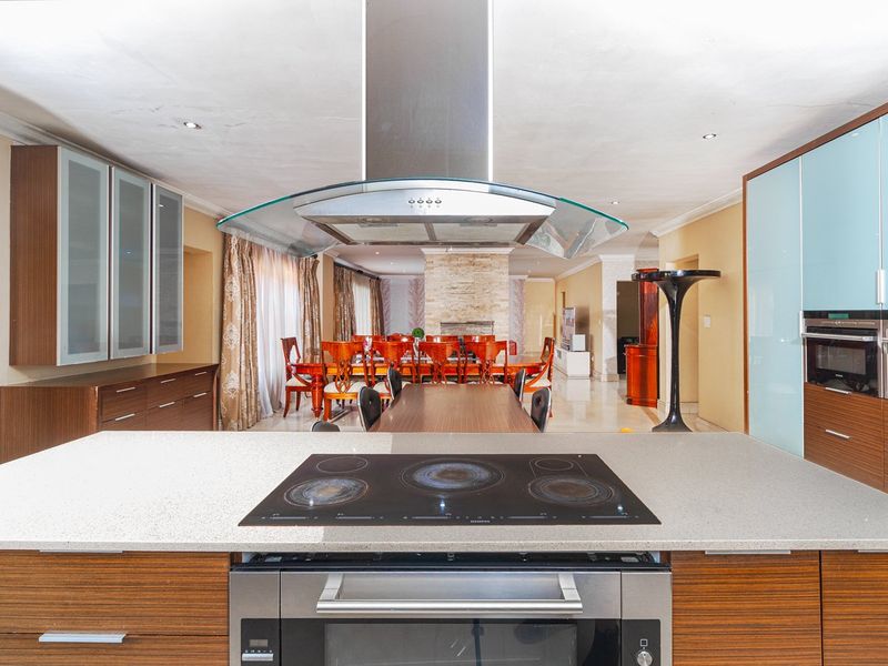 Spacious open-plan kitchen and dining area featuring a central island with integrated cooktop, modern cabinetry, and a stone fireplace in the adjacent living space.