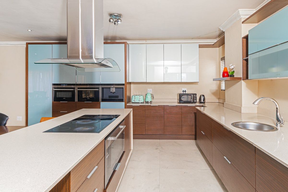 Modern kitchen featuring a large island with integrated hob, stone countertops, sleek wood-grain cabinetry, and high-end built-in appliances including an oven and coffee machine.