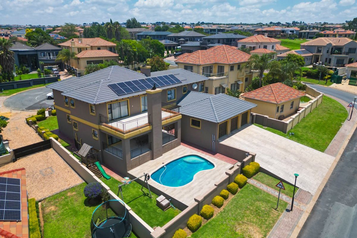 Aerial view of a residential property featuring a swimming pool, solar panels, tiled roof, and a paved driveway within a suburban estate.