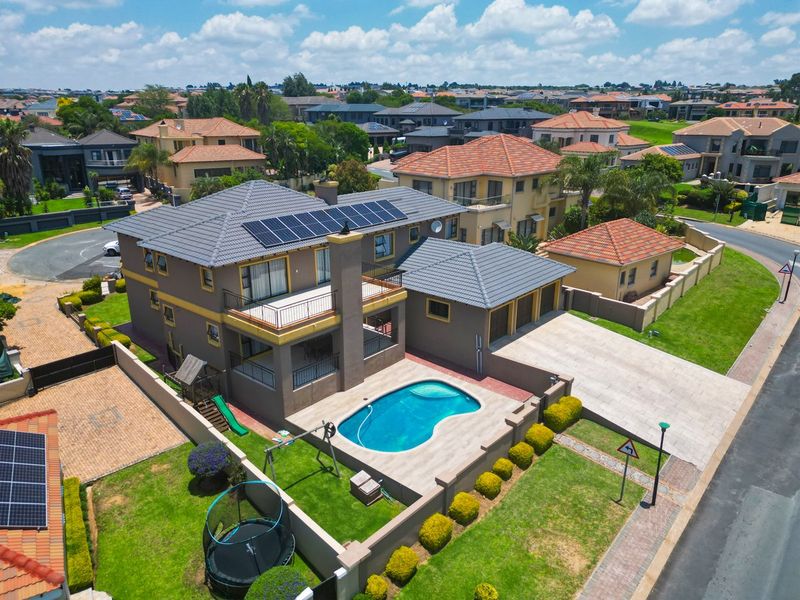 Aerial view of a residential property featuring a swimming pool, solar panels, tiled roof, and a paved driveway within a suburban estate.