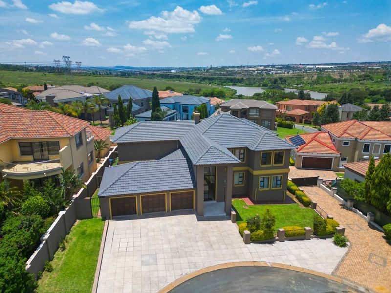 Aerial view of a modern double-story residential property featuring a triple garage, paved driveway, and well-maintained garden in a suburban estate setting.