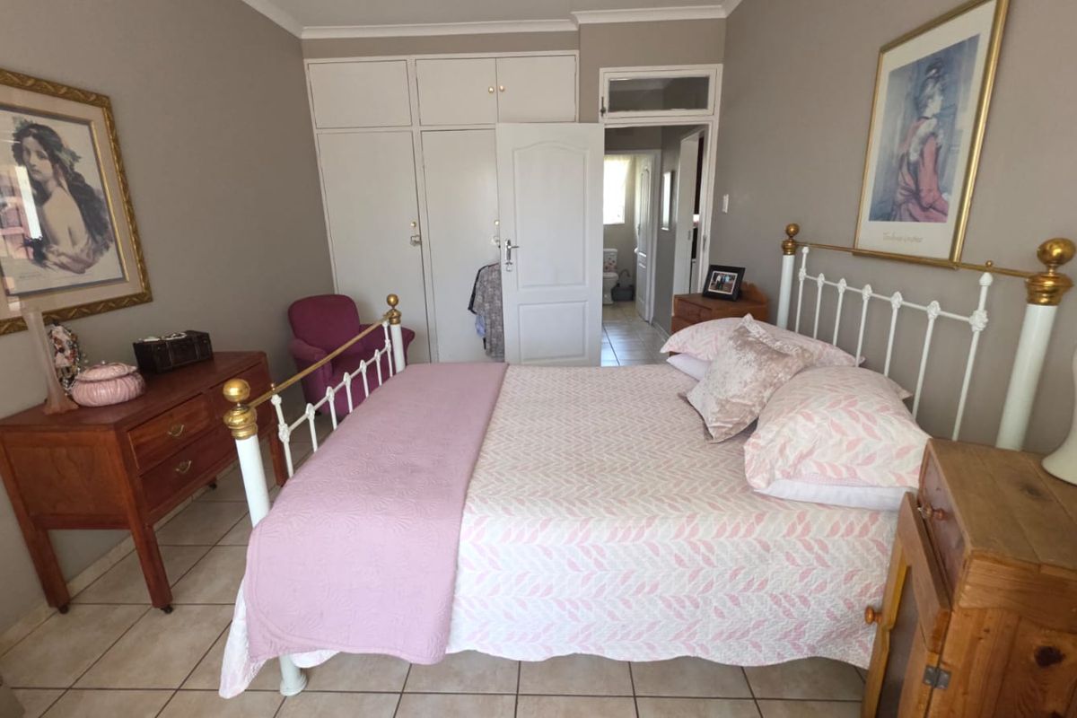 A bedroom featuring tiled flooring and built-in cupboards, with an adjoining view into a hallway and bathroom area.