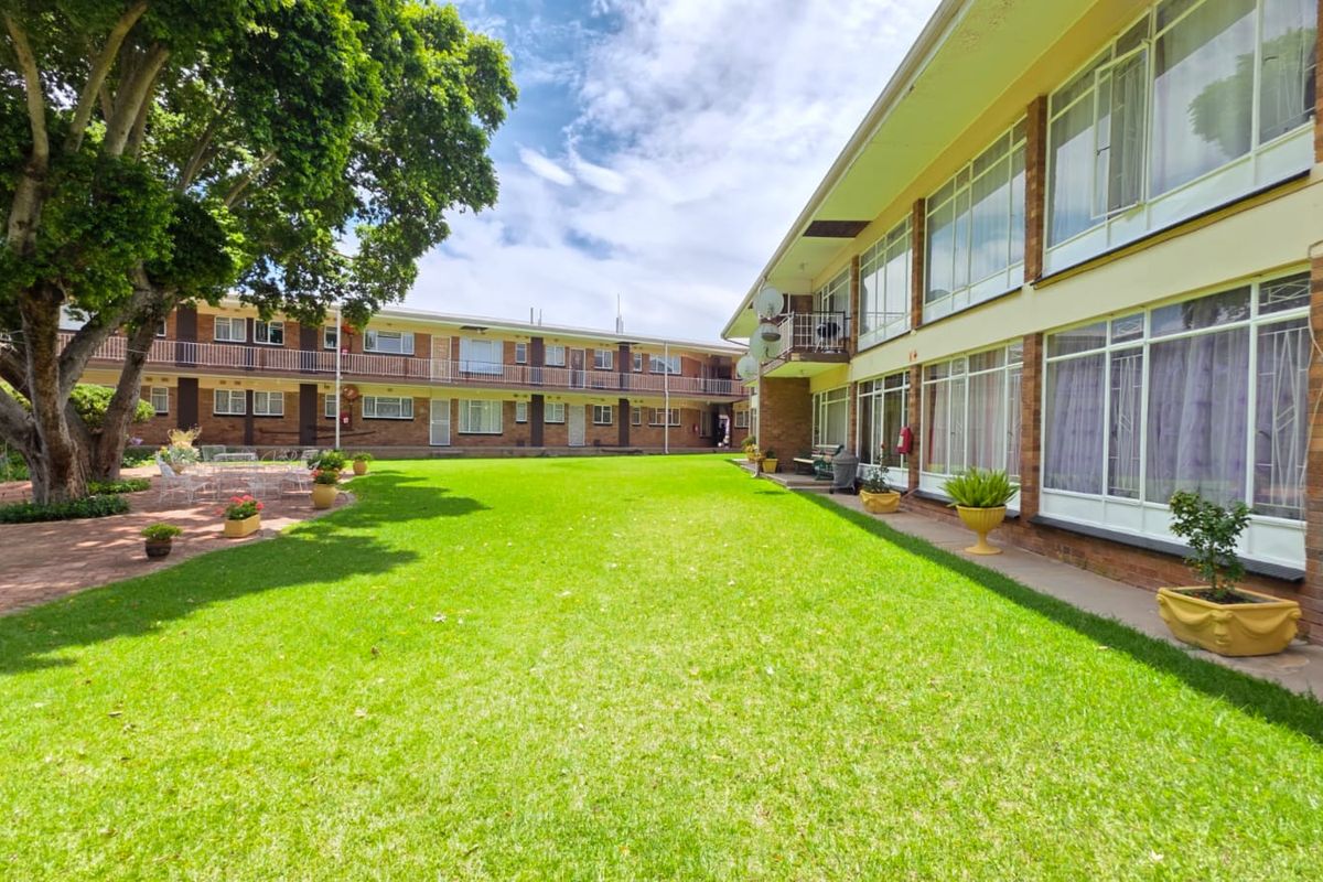 A view of the apartment complex exterior featuring a large communal lawn, brick facade, and multiple levels of balconies with large windows.