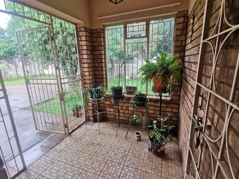 A covered patio area featuring exposed brick walls, tiled flooring, and secure metal security gates overlooking the garden.