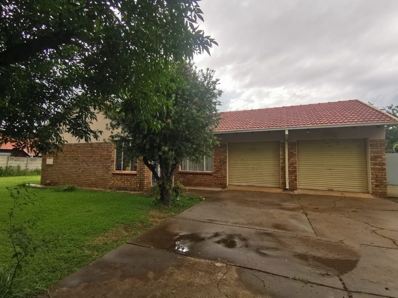 Front exterior view of a single-story brick house featuring a double garage, concrete driveway, and established front garden.