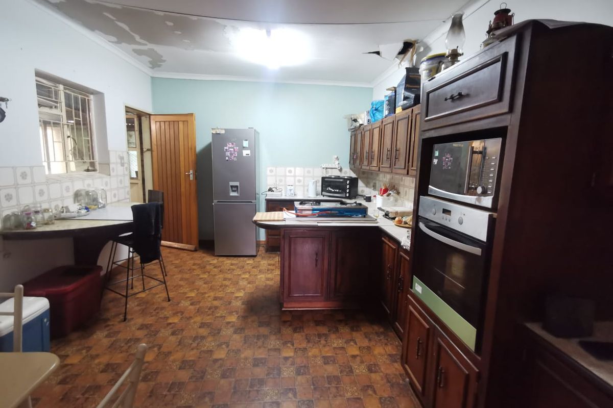 A dated kitchen featuring dark wood cabinetry, built-in oven, and tiled backsplash, requiring cosmetic updates to the ceiling and flooring.