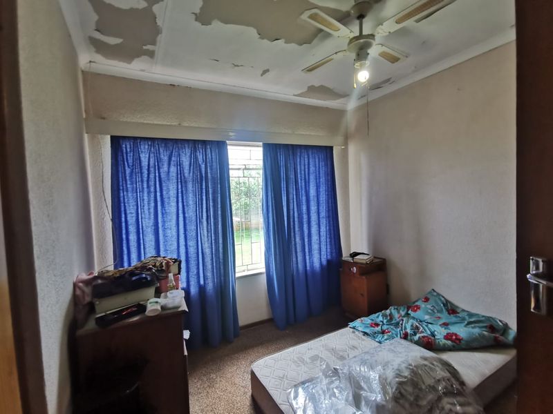 A bedroom featuring a ceiling fan and window with security bars, requiring cosmetic updates to the ceiling and flooring.