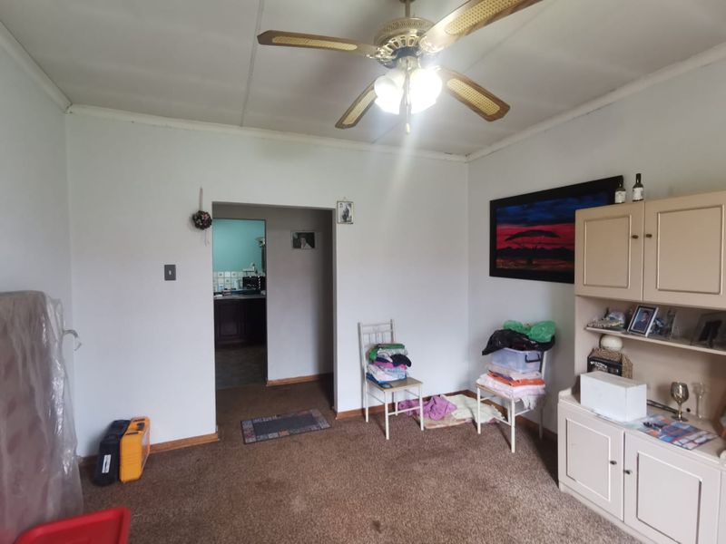 A living room area featuring a ceiling fan and direct access to the kitchen, with carpeted flooring and neutral wall finishes.