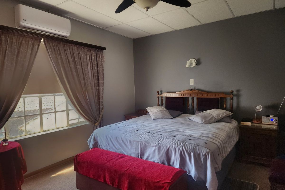 A bedroom featuring a wall-mounted air conditioning unit, a ceiling fan, and a window with curtains.