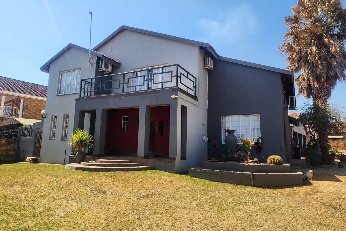 A two-story residential home featuring a covered patio, a balcony with metal railings, and a landscaped garden area.