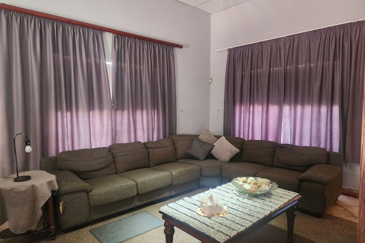 A living room featuring tiled flooring, neutral wall finishes, and large windows covered by curtains.