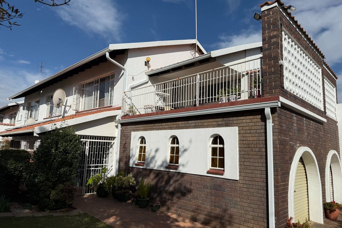 Rear view of a townhouse featuring a brick facade, an upper-level balcony with metal railings, and a paved walkway leading to the entrance.