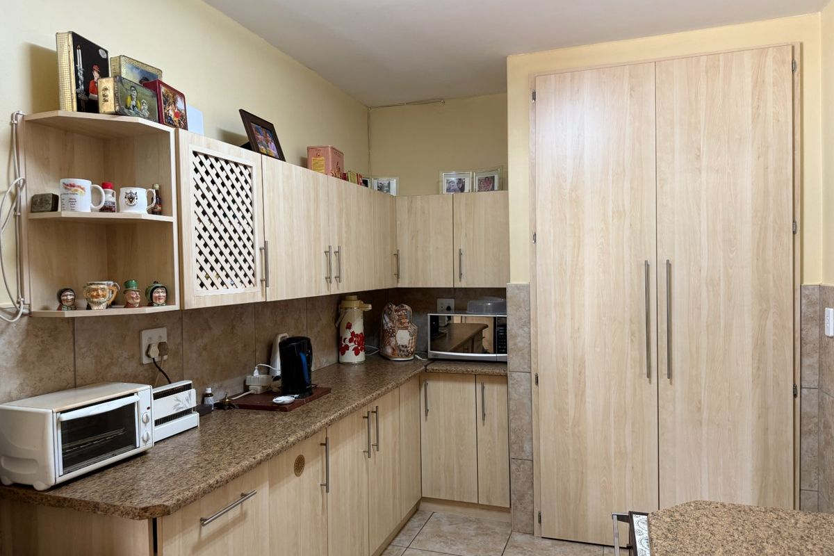 A functional kitchen featuring light wood-look laminate cabinetry, granite countertops, tiled backsplash, and a tall built-in pantry cupboard for ample storage.