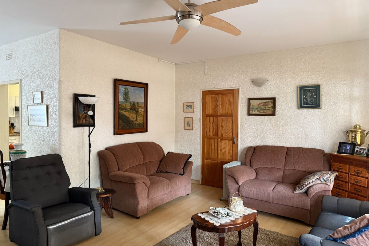 A comfortable living room featuring laminate flooring, a ceiling fan, and a classic timber door, offering a functional and well-maintained living space.