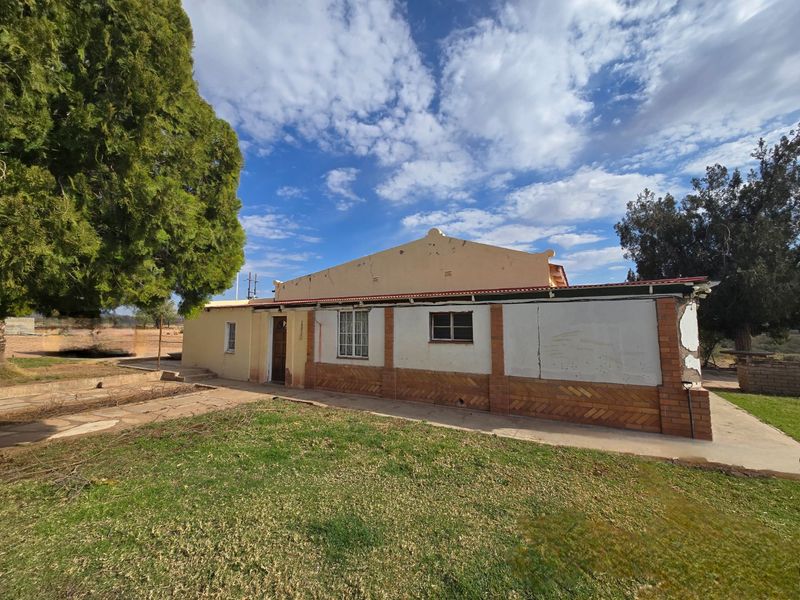 Rear view of a single-story house featuring a concrete patio, brick detailing, and visible exterior maintenance requirements.