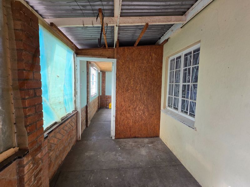 A covered outdoor patio area featuring exposed timber rafters, brickwork, and concrete flooring, currently requiring renovation and finishing to improve its structural and aesthetic appeal.