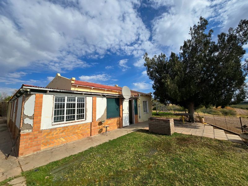 Rear view of the property featuring a paved patio area, a built-in brick braai, and exterior walls showing signs of wear and maintenance needs.