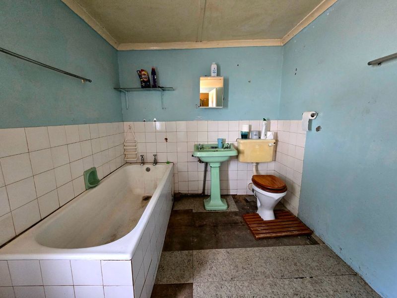 A dated bathroom featuring a pedestal basin, bathtub, and toilet, requiring significant renovation and modernization of fixtures and finishes.