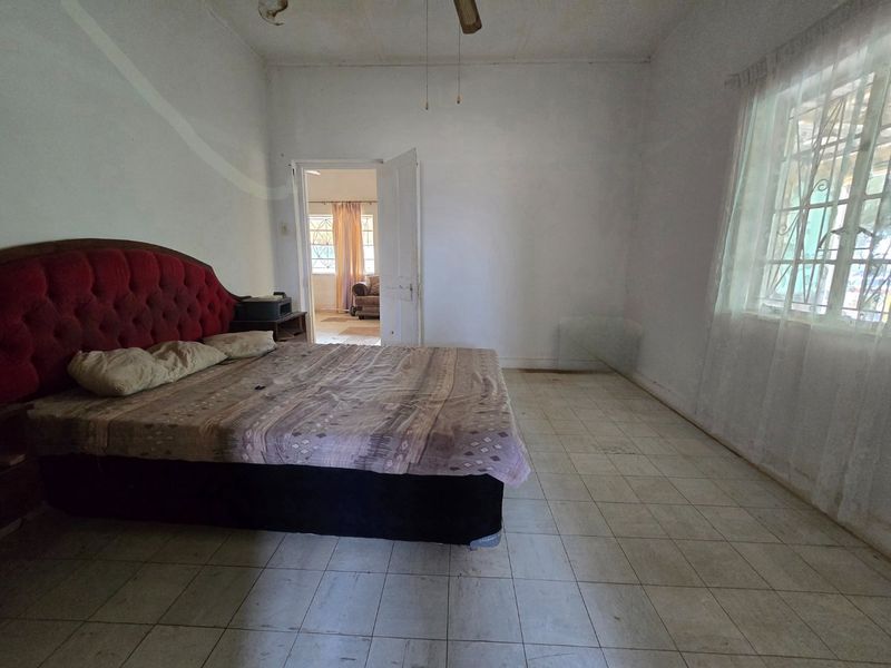 A spacious bedroom featuring tiled flooring, a ceiling fan, and security bars on the window, offering a blank canvas for potential renovation and modernization.