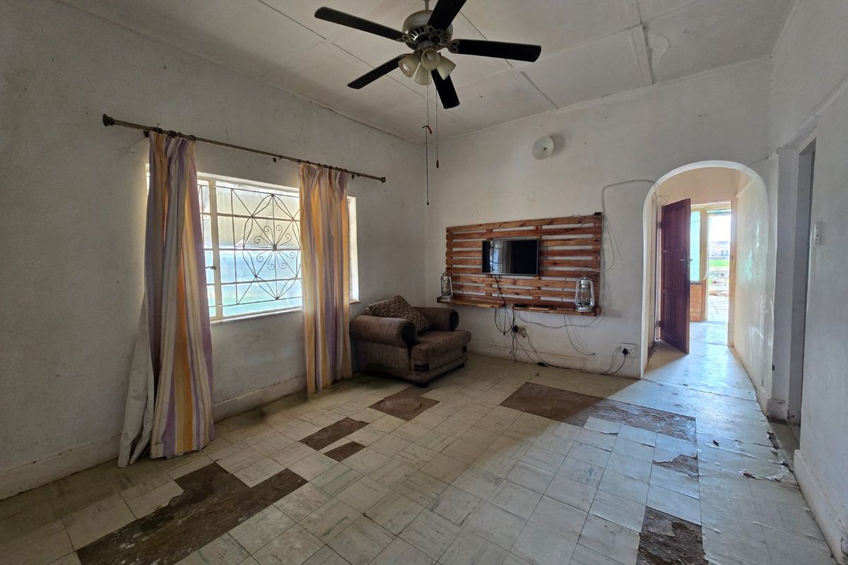 A living room featuring a ceiling fan, tiled flooring, and an arched doorway leading to an adjacent space, currently requiring significant cosmetic renovation.