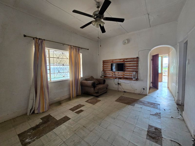 A living room featuring a ceiling fan, tiled flooring, and an arched doorway leading to an adjacent space, currently requiring significant cosmetic renovation.