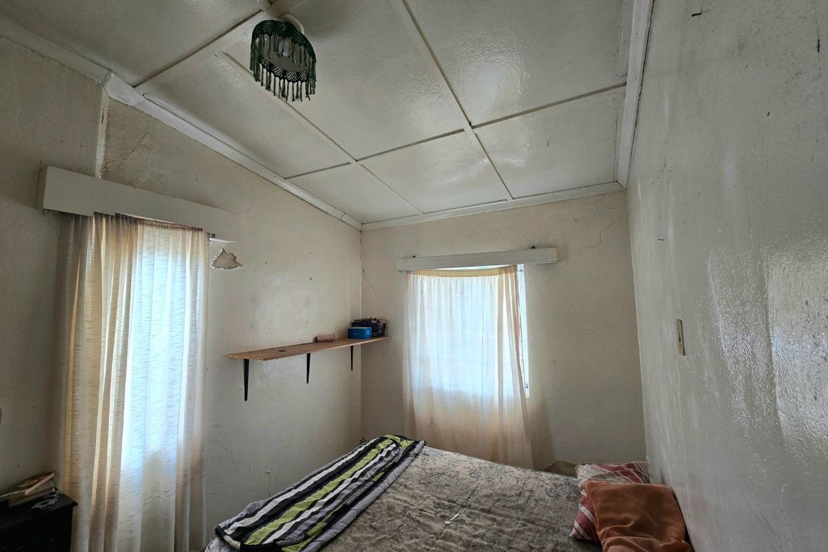 A bedroom featuring a tiled ceiling and built-in wall shelving, currently showing significant signs of wear including cracked plaster and peeling paint.