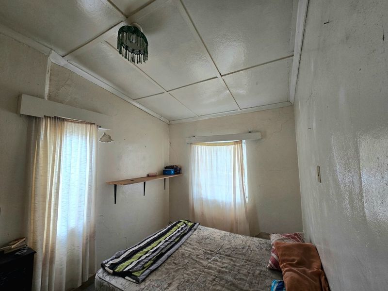 A bedroom featuring a tiled ceiling and built-in wall shelving, currently showing significant signs of wear including cracked plaster and peeling paint.
