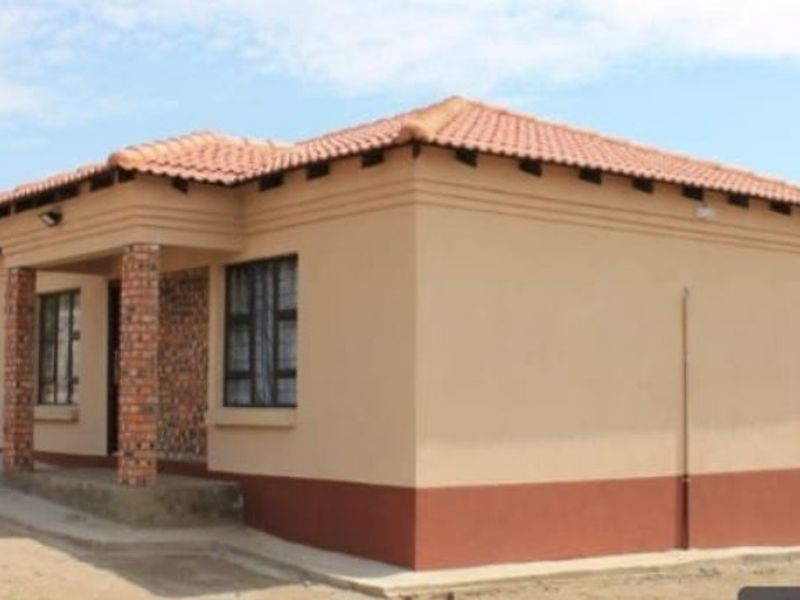 A single-story residential house featuring a terracotta tiled roof, plastered exterior walls with a contrasting base, and brick-accented entrance pillars.
