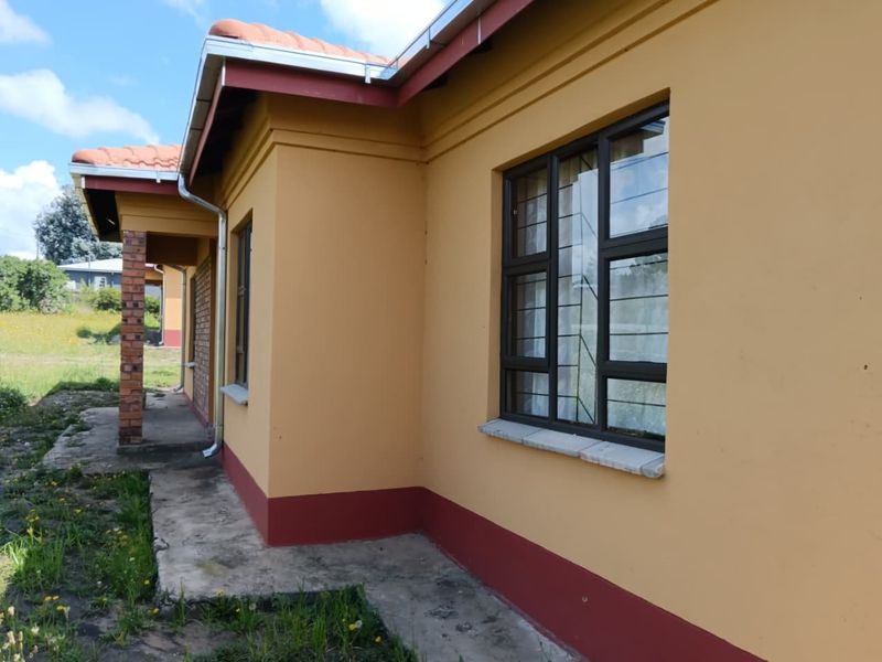Side view of the house featuring yellow painted exterior walls, terracotta roof tiles, aluminium window frames with security bars, and a concrete walkway.