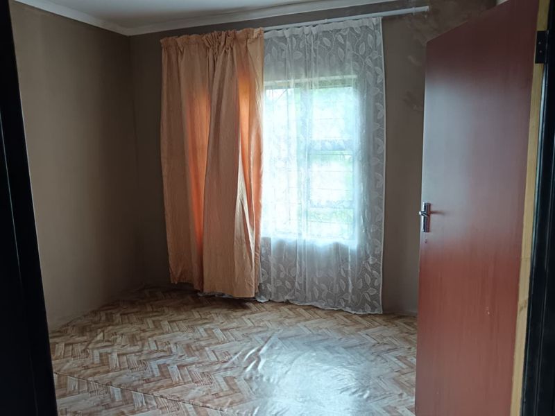An empty bedroom featuring herringbone pattern vinyl flooring and a window fitted with security bars.