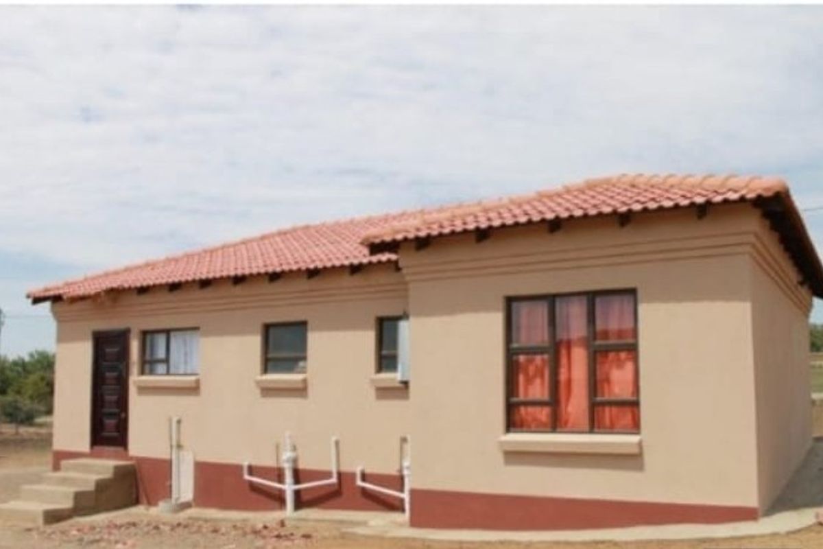 A view of the rear exterior of a single-story house featuring terracotta roof tiles, plastered walls, and external plumbing fixtures.