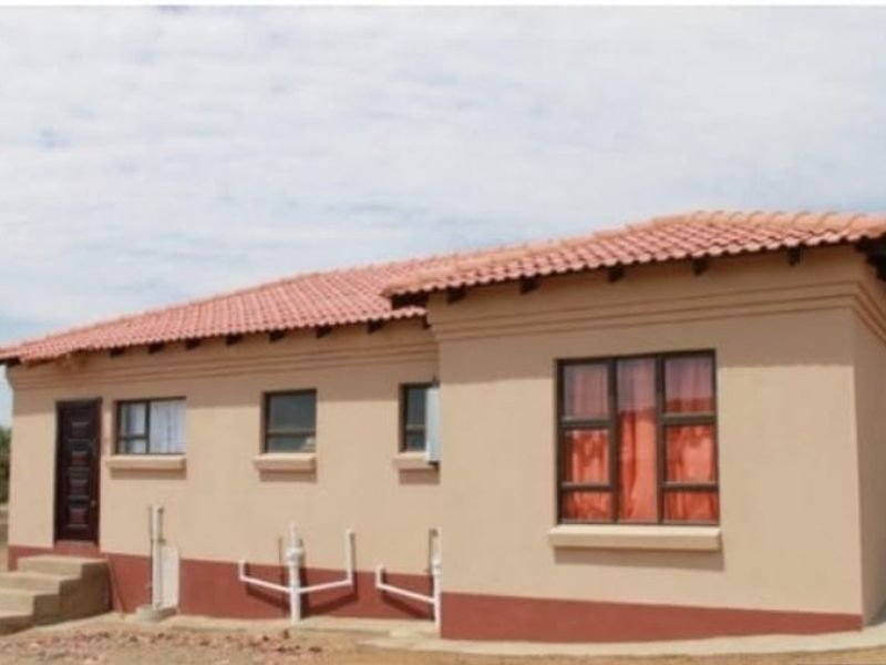 A view of the rear exterior of a single-story house featuring terracotta roof tiles, plastered walls, and external plumbing fixtures.