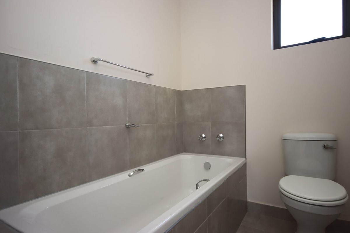 A clean, modern bathroom featuring a built-in bathtub with grey tiled splashback and a standard toilet.